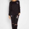 Black sweat suit with ripped knee detail, comfortable loungewear. Soft, textured fabric, visible stitching. Casual, stylish.