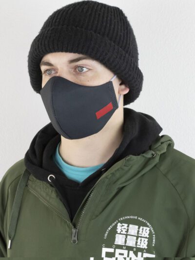 Close-up of a black face mask. Woven label detail. Finely stitched, durable fabric texture. Washable, reusable cloth face cov