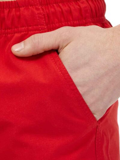 Lightweight summer beach shorts in a vibrant coral hue. Fine stitching detail shows durable construction. Soft, textured fabr