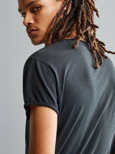 Stack of premium blank t-shirts in various muted colors, close-up showing fine-gauge knit fabric and durable double-needle st