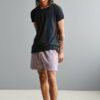 Stack of premium blank t-shirts in various muted colors, close-up showing fine-gauge knit fabric and durable double-needle st