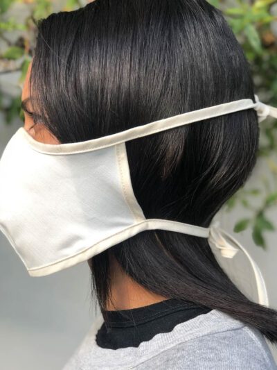 Close-up of a breathable cotton face mask. Soft fabric texture, neat stitching. Reusable face covering, light color, comforta