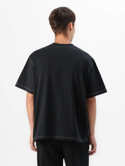 Black oversized t-shirt with contrast white stitching, drop shoulders, pocket. Soft, textured fabric. Custom logo imprint are