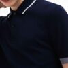 Close-up of a finely knit polo shirt, hints of navy and white. Sharp collar, clean stitching. Classic menswear garment detail