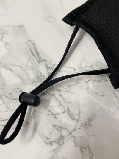 Close-up of a breathable three-layer face mask, charcoal gray color, showcasing fine stitching, adjustable ear loops, and a s