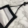 Close-up of a breathable three-layer face mask, charcoal gray color, showcasing fine stitching, adjustable ear loops, and a s