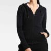 Black tracksuit featuring a hooded jacket with a visible zipper and matching pants. Fine stitching and soft-looking fabric te