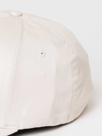 Close-up of a customizable twill cap. Visible stitching details, slightly distressed look, neutral tone. Garment is soft and